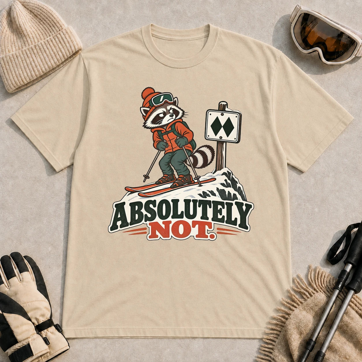 Sand tee featuring a wary raccoon skier beside a double black diamond trail sign above the phrase “Absolutely Not.”