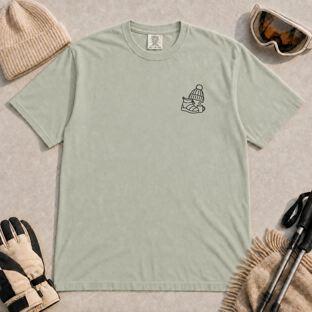 Bay tee featuring a minimalist black line-art design of a ski boot, winter beanie, and steaming mug on the left chest.