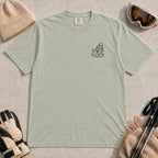 Bay tee featuring a minimalist black line-art design of a ski boot, winter beanie, and steaming mug on the left chest.