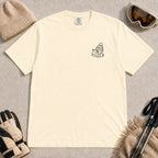 Ivory tee featuring a minimalist black line-art design of a ski boot, winter beanie, and steaming mug on the left chest.