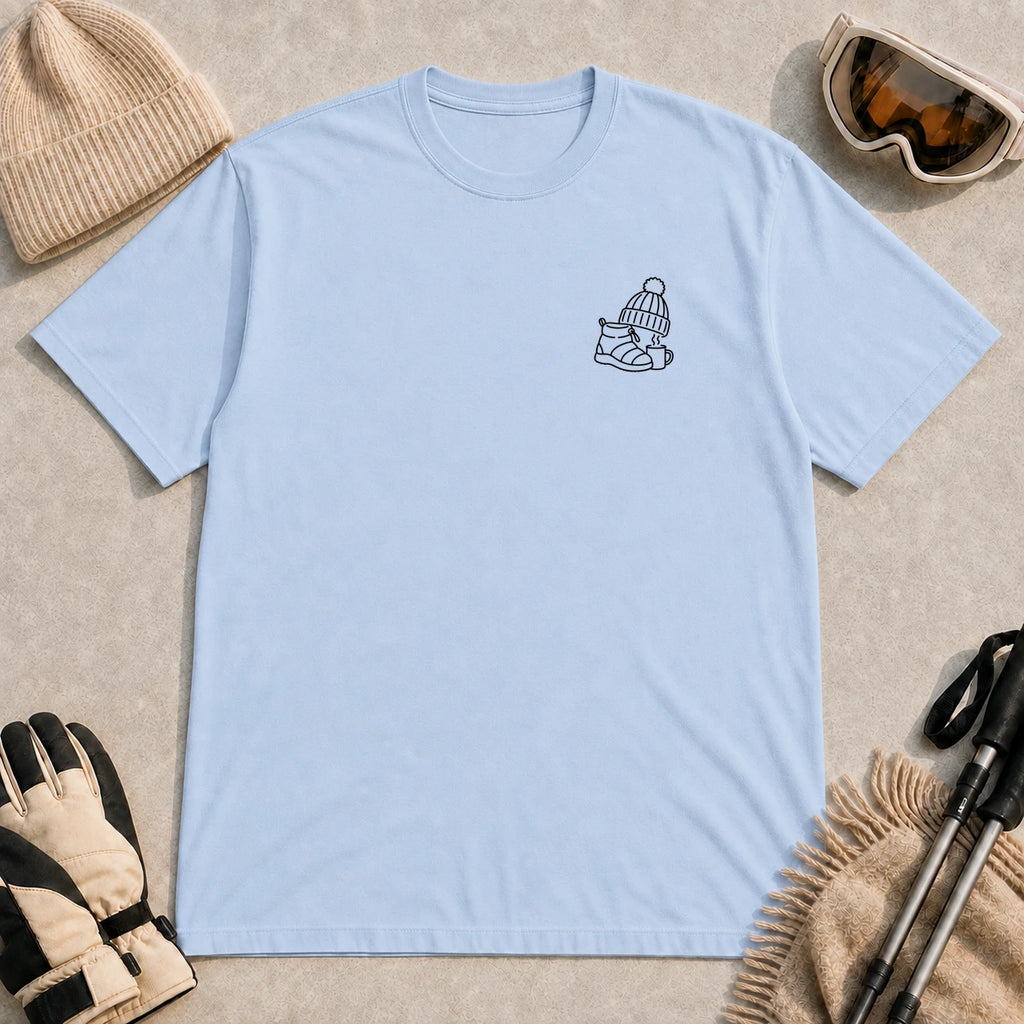 Light Blue tee featuring a minimalist black line-art design of a ski boot, winter beanie, and steaming mug on the left chest.