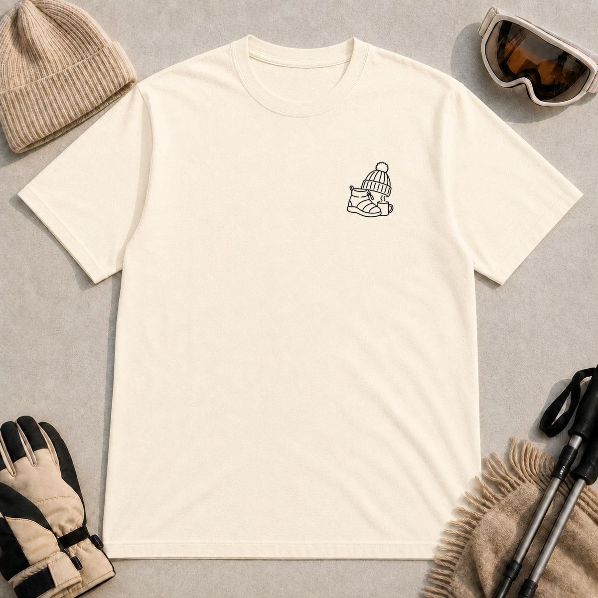 Natural tee featuring a minimalist black line-art design of a ski boot, winter beanie, and steaming mug on the left chest.