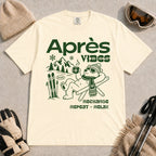 Ivory tee featuring a relaxed bear in sunglasses holding a steaming mug beside skis, with retro green “Après Vibes” and “Recharge, Repeat – Relax” text.