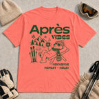 Coral Silk tee featuring a relaxed bear in sunglasses holding a steaming mug beside skis, with retro green “Après Vibes” and “Recharge, Repeat – Relax” text.