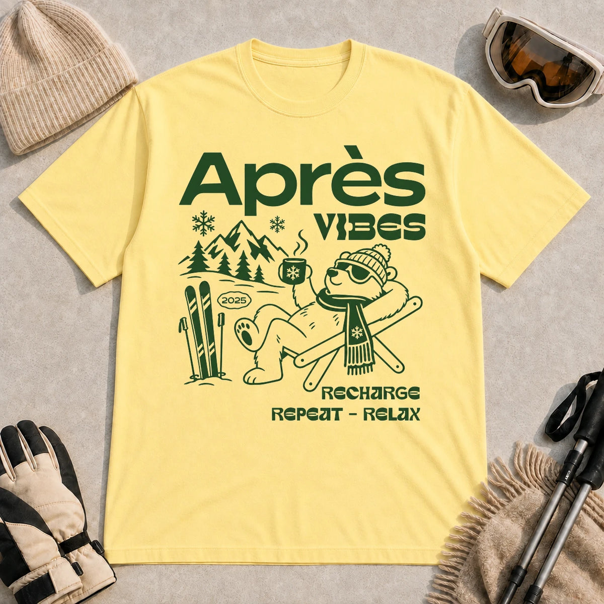 Cornsilk tee featuring a relaxed bear in sunglasses holding a steaming mug beside skis, with retro green “Après Vibes” and “Recharge, Repeat – Relax” text.
