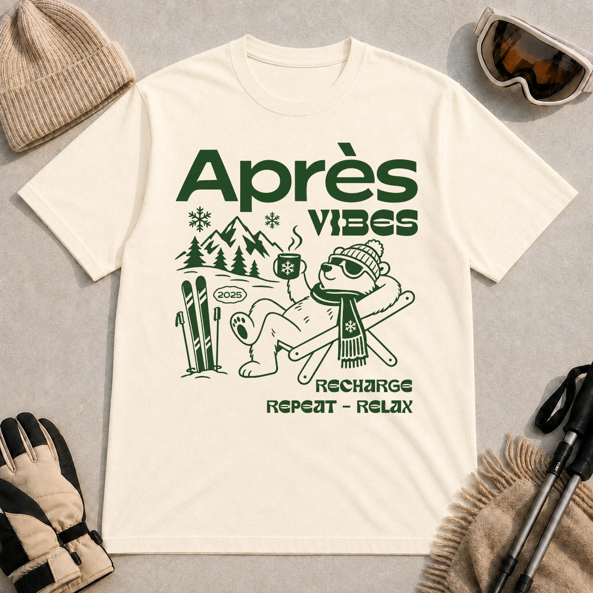 Natural tee featuring a relaxed bear in sunglasses holding a steaming mug beside skis, with retro green “Après Vibes” and “Recharge, Repeat – Relax” text.