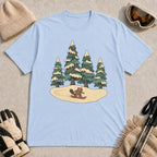 Light Blue t-shirt featuring a beaver snowboarding through a snowy clearing beneath tall pine trees.