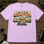 Orchid tee featuring a bunny sitting on a mountain overlook surrounded by retro sunset, pine, and alpine scenery, with the phrase “Better Up Here.”