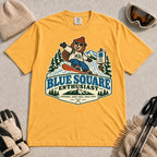 Mustard tee featuring a cheerful bear snowboarding past a blue-square trail sign above the phrase “Blue Square Enthusiast” with “Groomers. Good Vibes. More Runs.”