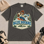 Pepper tee featuring a cheerful bear snowboarding past a blue-square trail sign above the phrase “Blue Square Enthusiast” with “Groomers. Good Vibes. More Runs.”