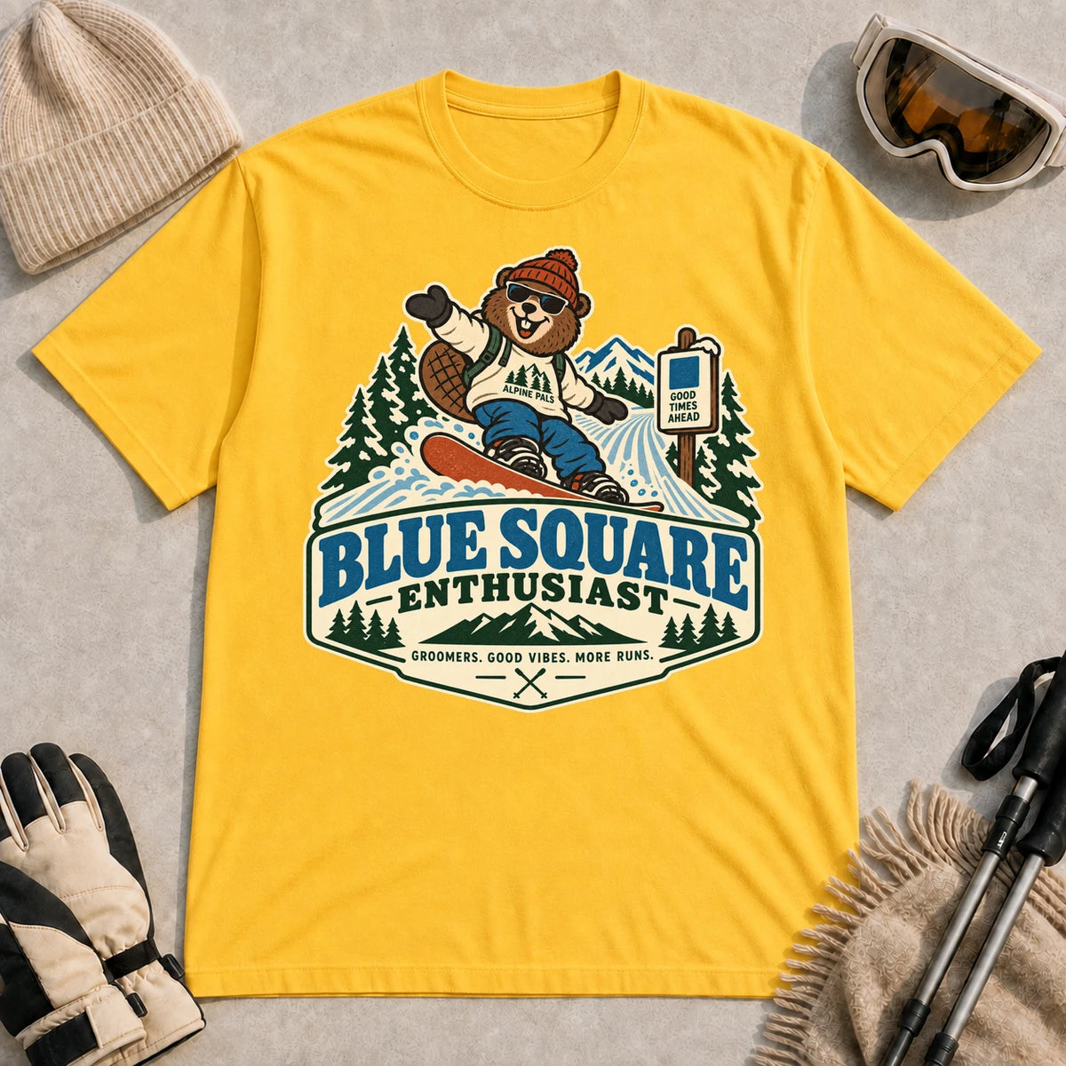 Daisy tee featuring a cheerful bear snowboarding past a blue-square trail sign above the phrase “Blue Square Enthusiast” with “Groomers. Good Vibes. More Runs.”