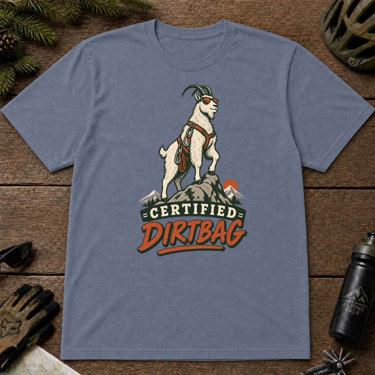 Heather Indigo tee featuring a sunglasses-wearing mountain goat in climbing gear standing on a rocky summit, with the phrase “Certified Dirtbag.”