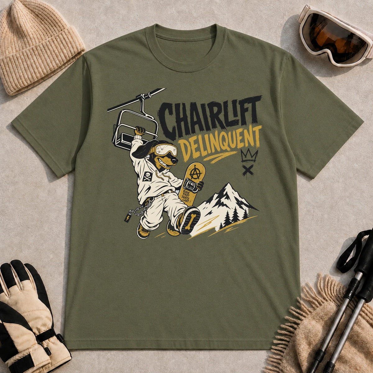 Military Green tee featuring a rebellious dog snowboarder hanging from a chairlift with a snowboard in hand, with the phrase “Chairlift Delinquent.”