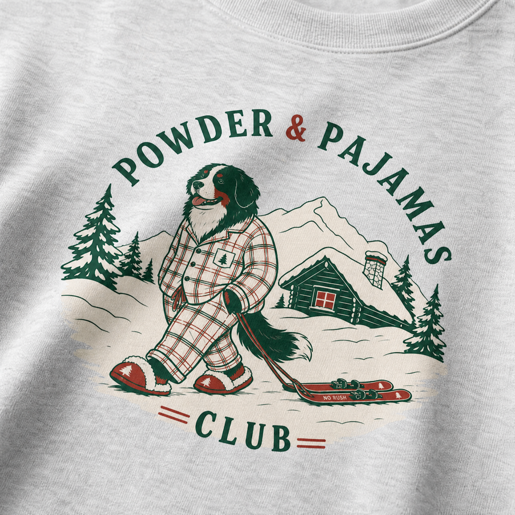 Ash gray sweatshirt with a graphic of a dog in plaid pajamas skiing, surrounded by trees and a cabin, with 'Powder & Pajamas Club' text.