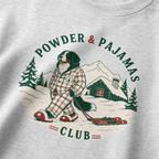Ash gray sweatshirt with a graphic of a dog in plaid pajamas skiing, surrounded by trees and a cabin, with 'Powder & Pajamas Club' text.