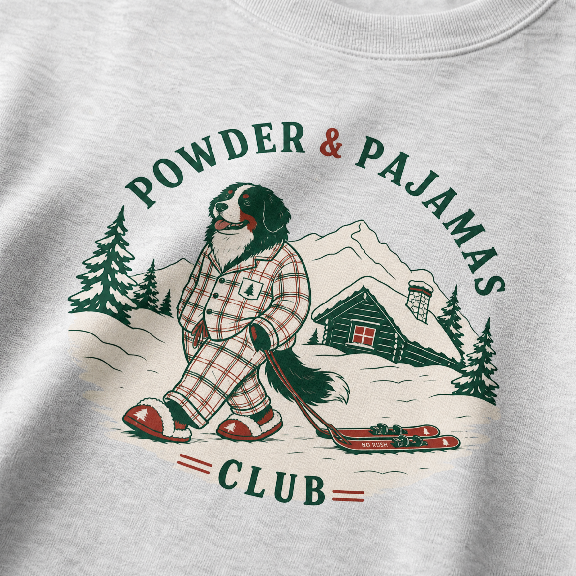 Ash gray sweatshirt with a graphic of a dog in plaid pajamas skiing, surrounded by trees and a cabin, with 'Powder & Pajamas Club' text.