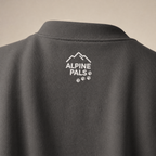 Charcoal gray sweatshirt with 'Alpine Pals' logo on the back against a beige background