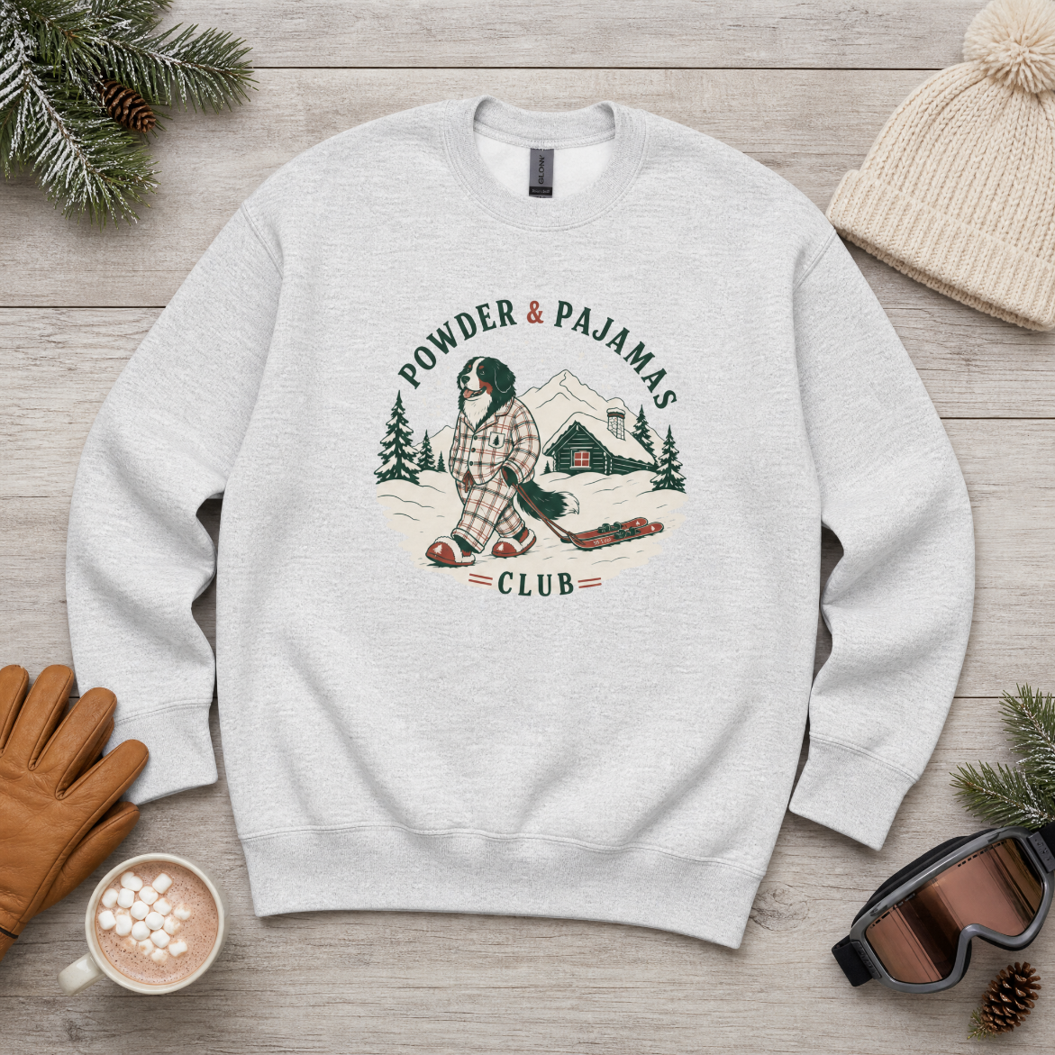 Ash gray sweatshirt with 'Powder & Pajamas Club' graphic on a wooden surface with winter accessories.