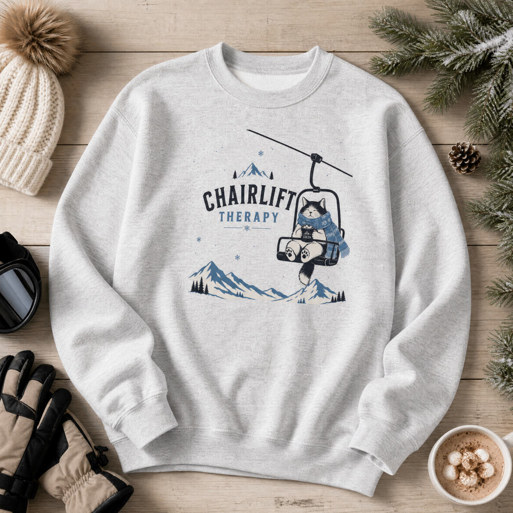 Ash gray sweatshirt with 'Chairlift Therapy' graphic on a wooden surface with winter accessories.