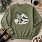Military green sweatshirt with a winter graphic and text on a wooden surface with winter accessories.