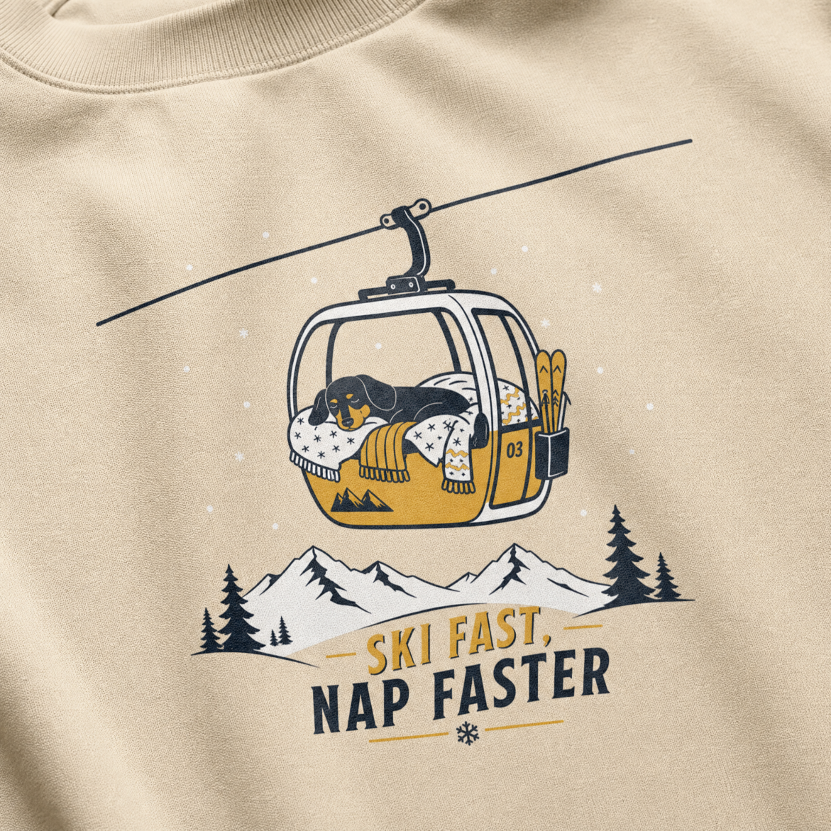 Sand colored sweatshirt with a graphic of a dog in a ski lift and mountain text 'Ski Fast, Nap Faster'.