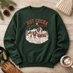 Forest green sweatshirt with 'Hot Cocoa Patrol' design on a wooden surface with winter accessories.