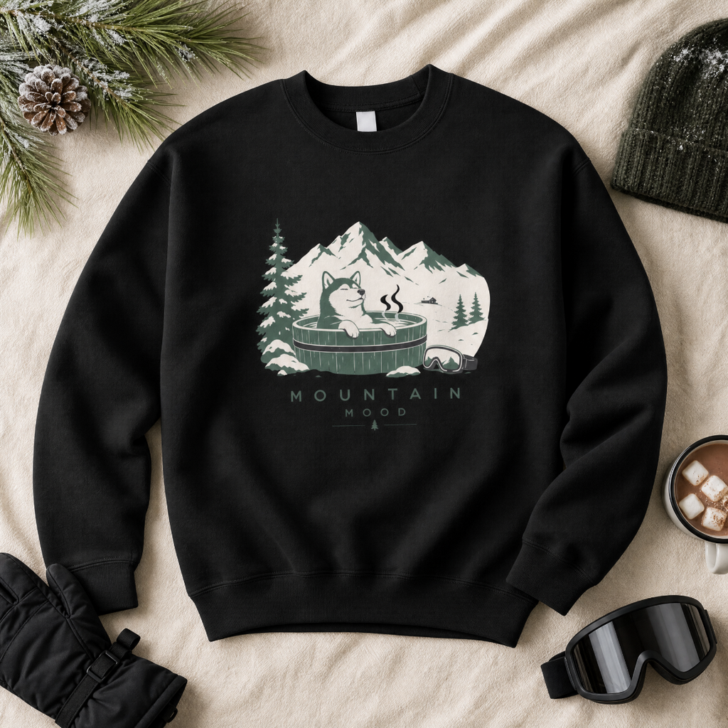 Black sweatshirt with mountain and cabin graphic on a beige surface with winter accessories.