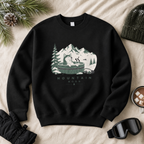 Black sweatshirt with mountain and cabin graphic on a beige surface with winter accessories.