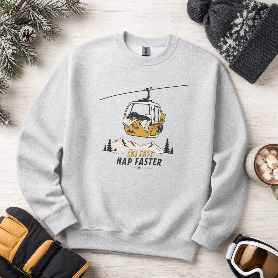 Sport gray sweatshirt with a ski lift graphic and text on a wooden surface with winter accessories.