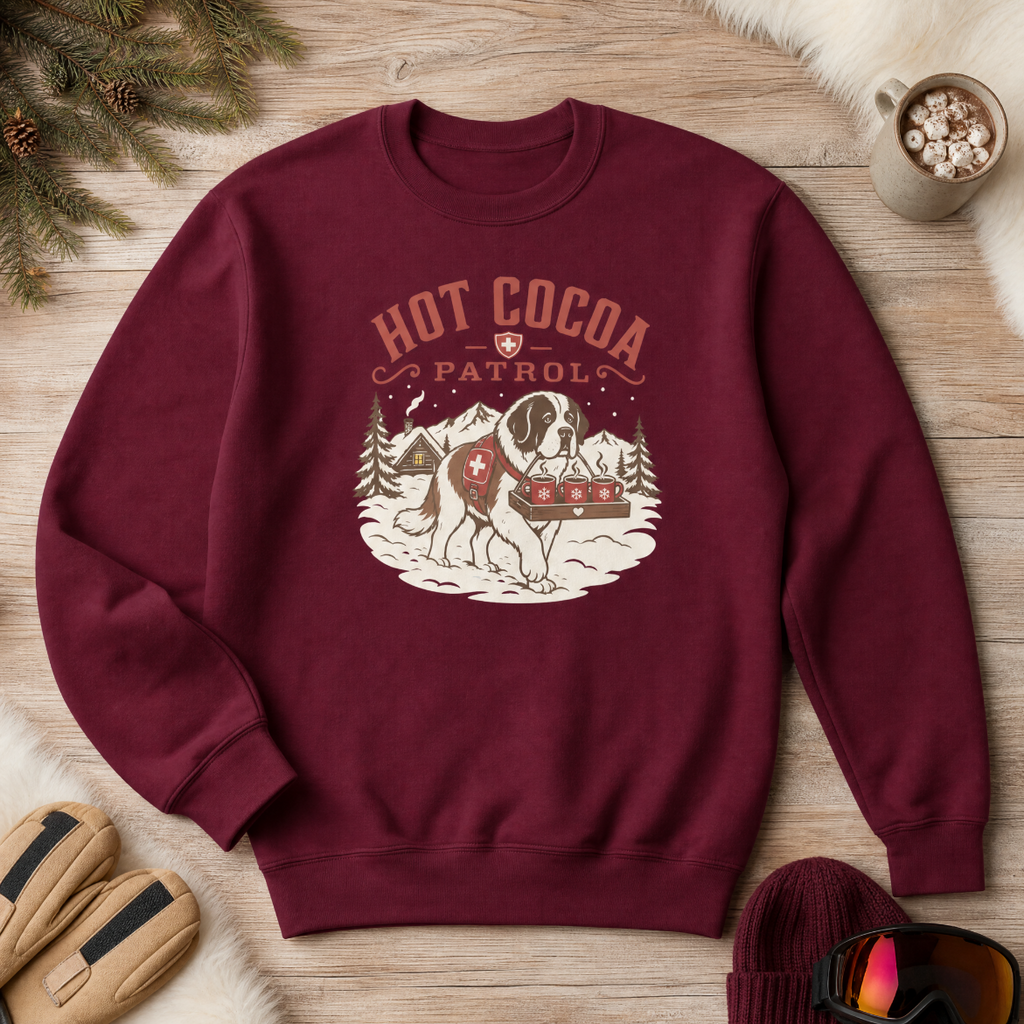 Maroon sweatshirt with 'Hot Cocoa Patrol' graphic on a wooden surface with winter accessories.