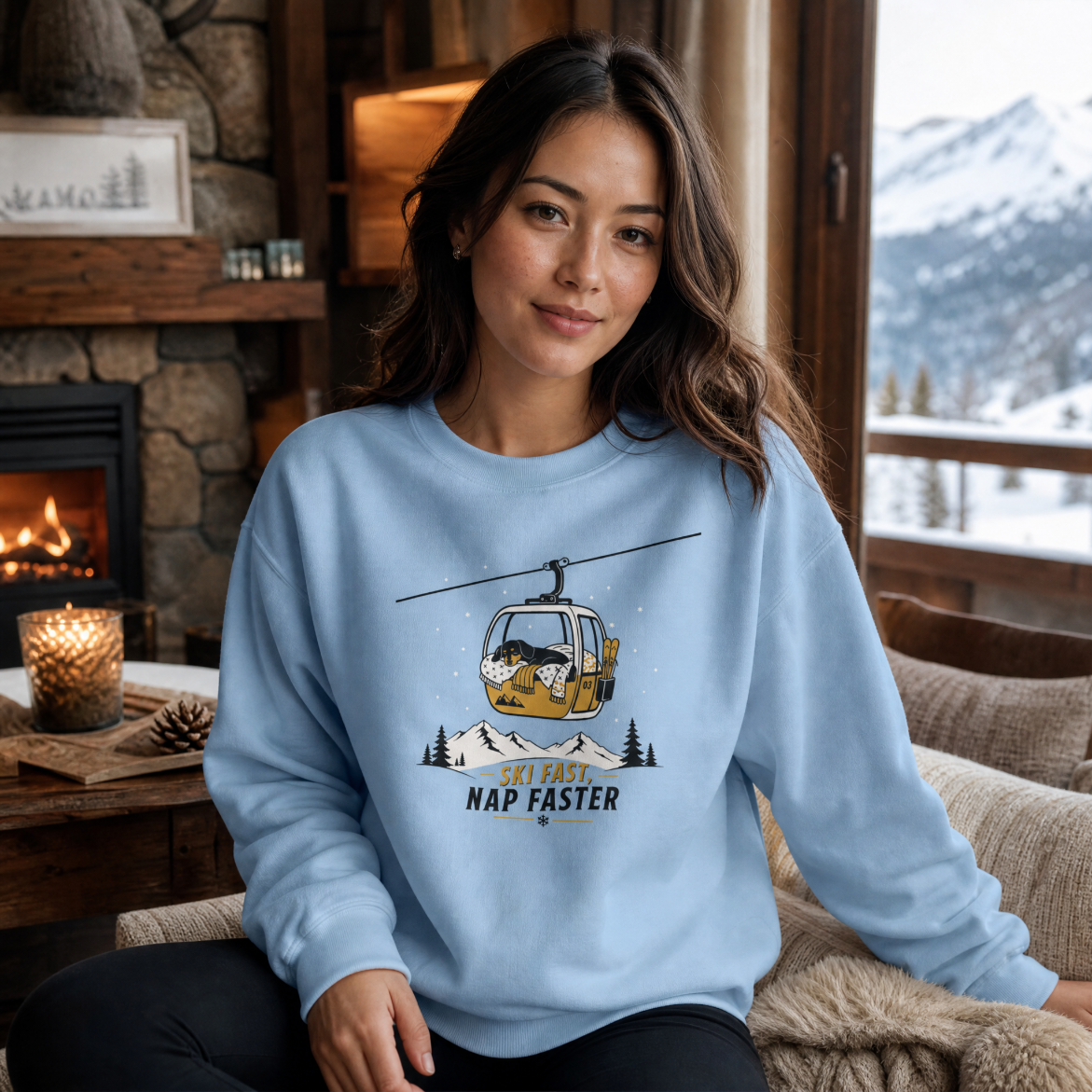Woman wearing a light blue sweatshirt with a graphic design, sitting in a cozy room with a fireplace and mountain view.