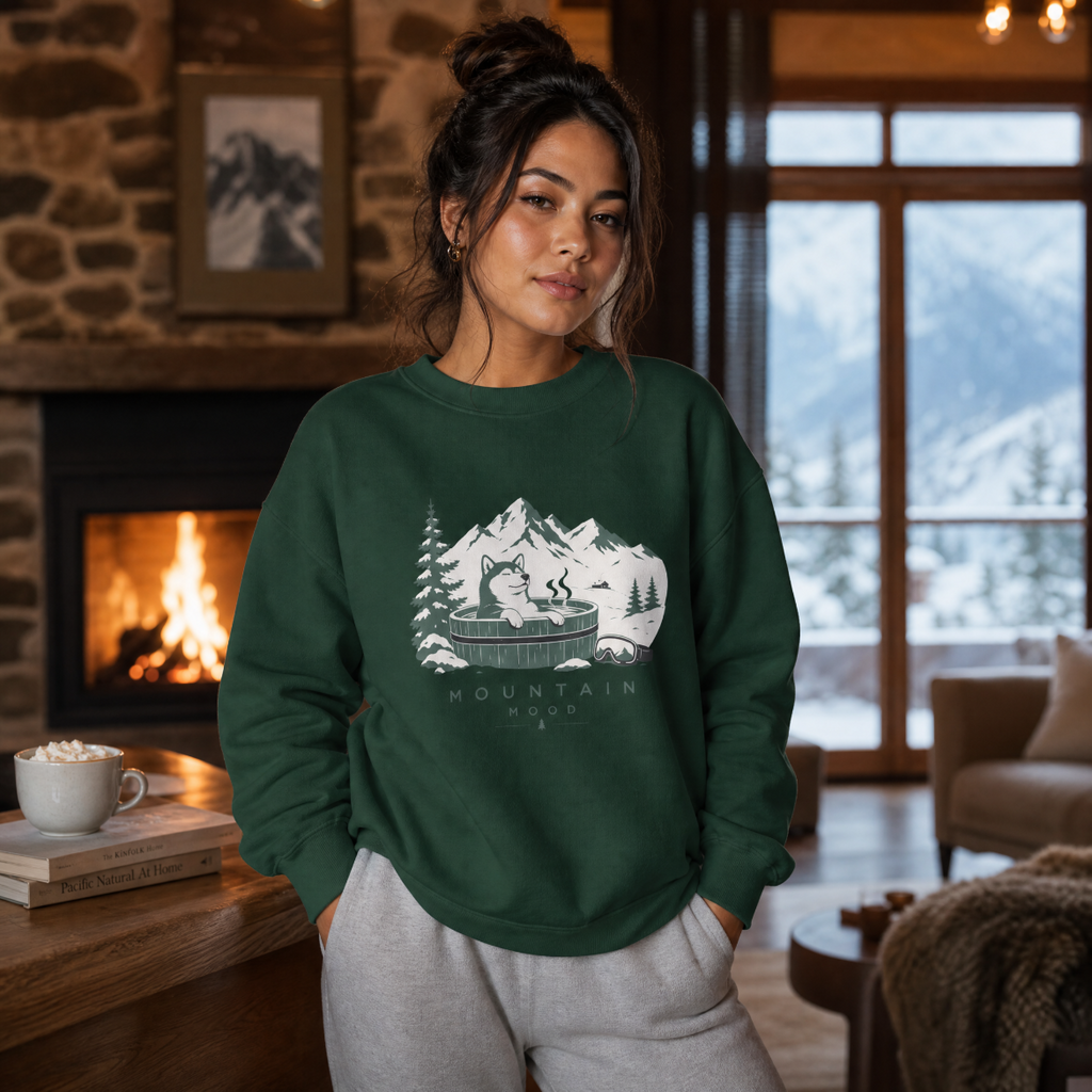 Woman wearing a forest green sweatshirt with a mountain design in a cozy living room.