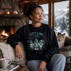Woman wearing a black sweatshirt with a graphic design, sitting in a cozy room with a fireplace and snowy window view.