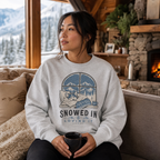 Woman wearing a sweater with a snowy design, sitting on a couch in a cozy room with a fireplace and mountain view.