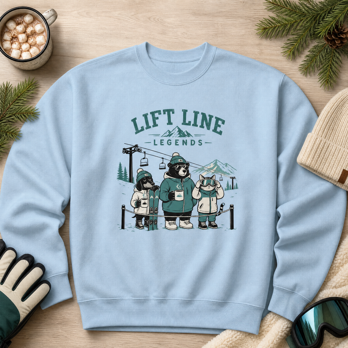 Light blue sweatshirt with cartoon bears and 'Lift Line Legends' text on a wooden surface with winter accessories.