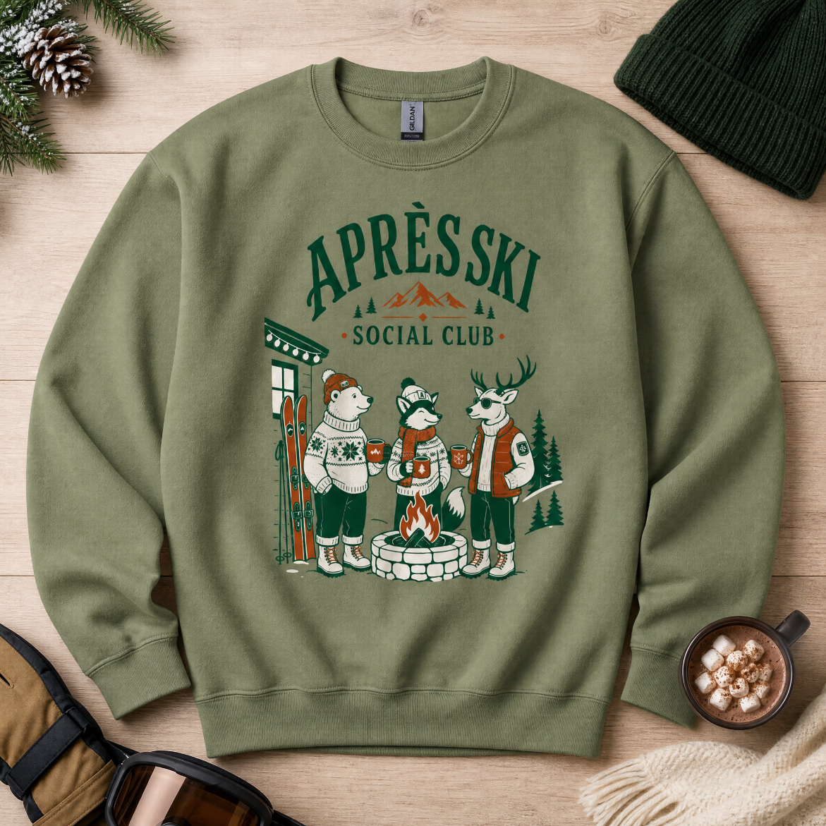 Military green sweatshirt with 'Apres Ski Social Club' design featuring animals around a campfire on a wooden surface.