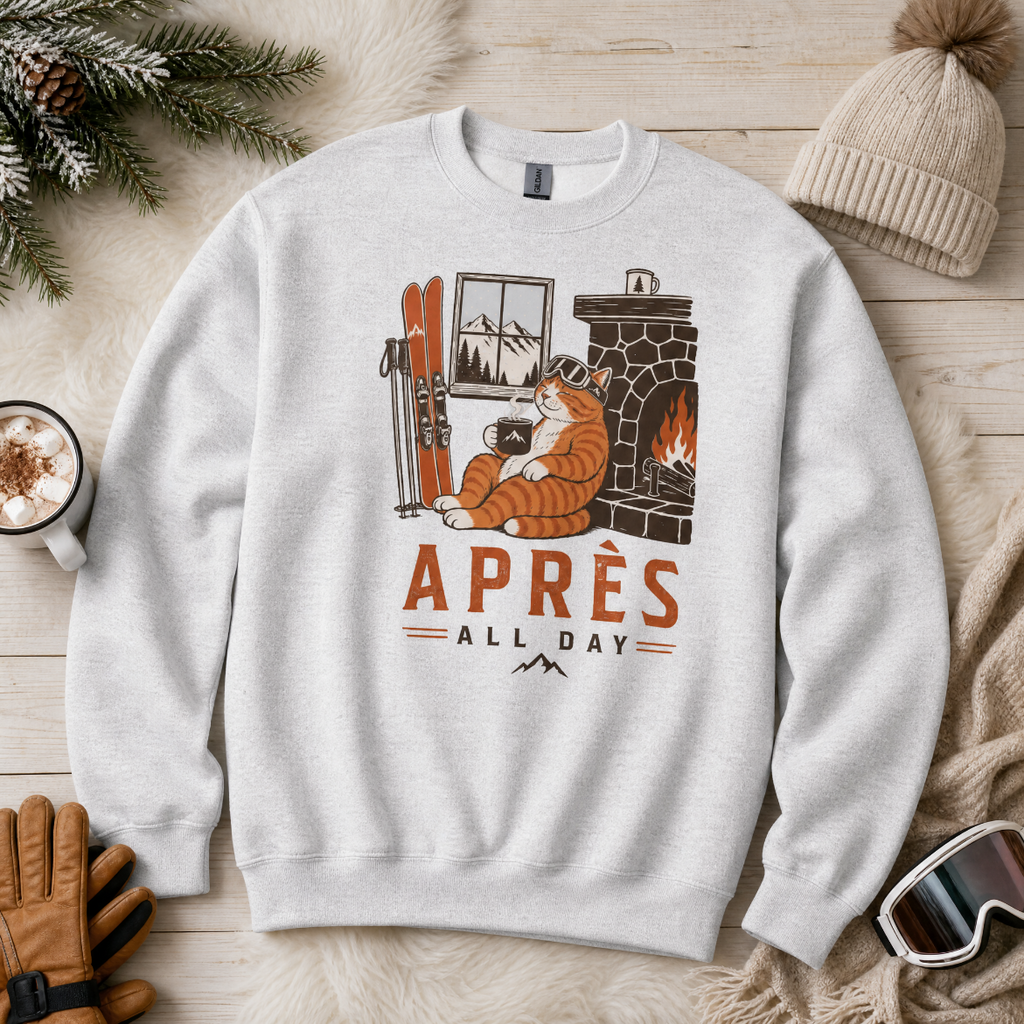 Ash gray sweatshirt with a fox graphic and 'APRES ALL DAY' text on a wooden surface with winter accessories.