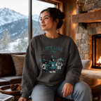 Woman wearing a sweatshirt with a ski lift and bear design, sitting in a cozy living room with a mountain view.
