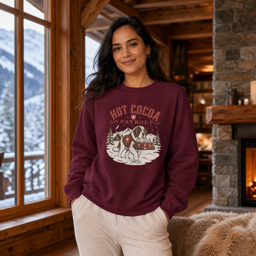 Woman wearing a maroon sweatshirt with 'Hot Cocoa Patrol' design in a cozy cabin setting.