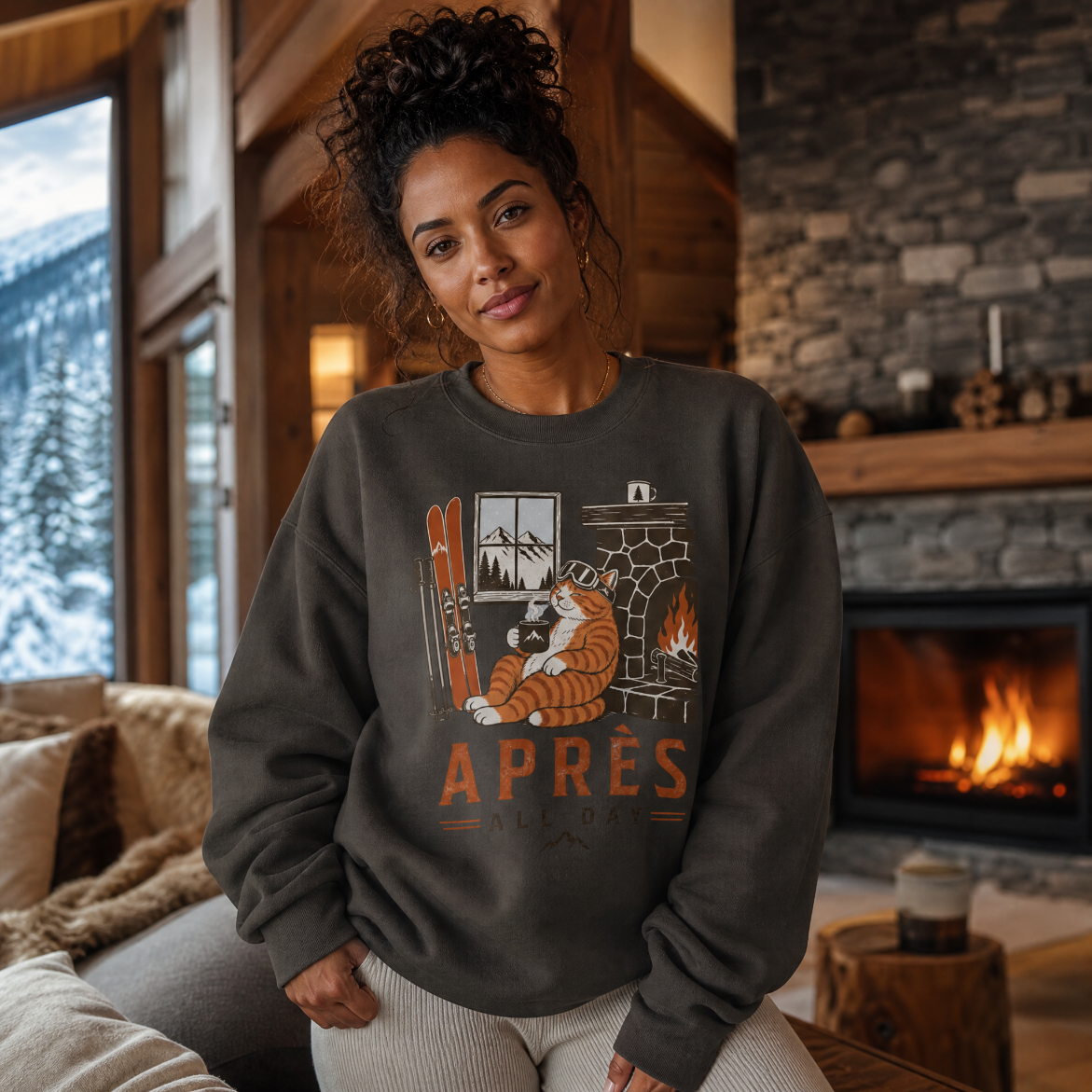 Woman wearing a sweater with a cat graphic and 'APRES' text in a cozy room with a fireplace.