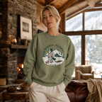 Woman wearing a military green sweatshirt with a graphic design in a cozy living room.