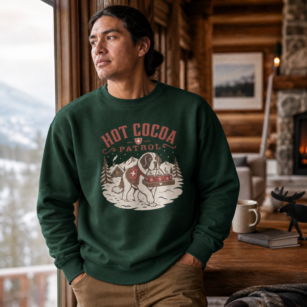 Man wearing a green sweatshirt with 'Hot Cocoa Patrol' design in a cozy cabin setting.
