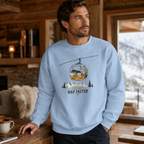 Man wearing a light blue sweatshirt with a graphic design in a cozy indoor setting.