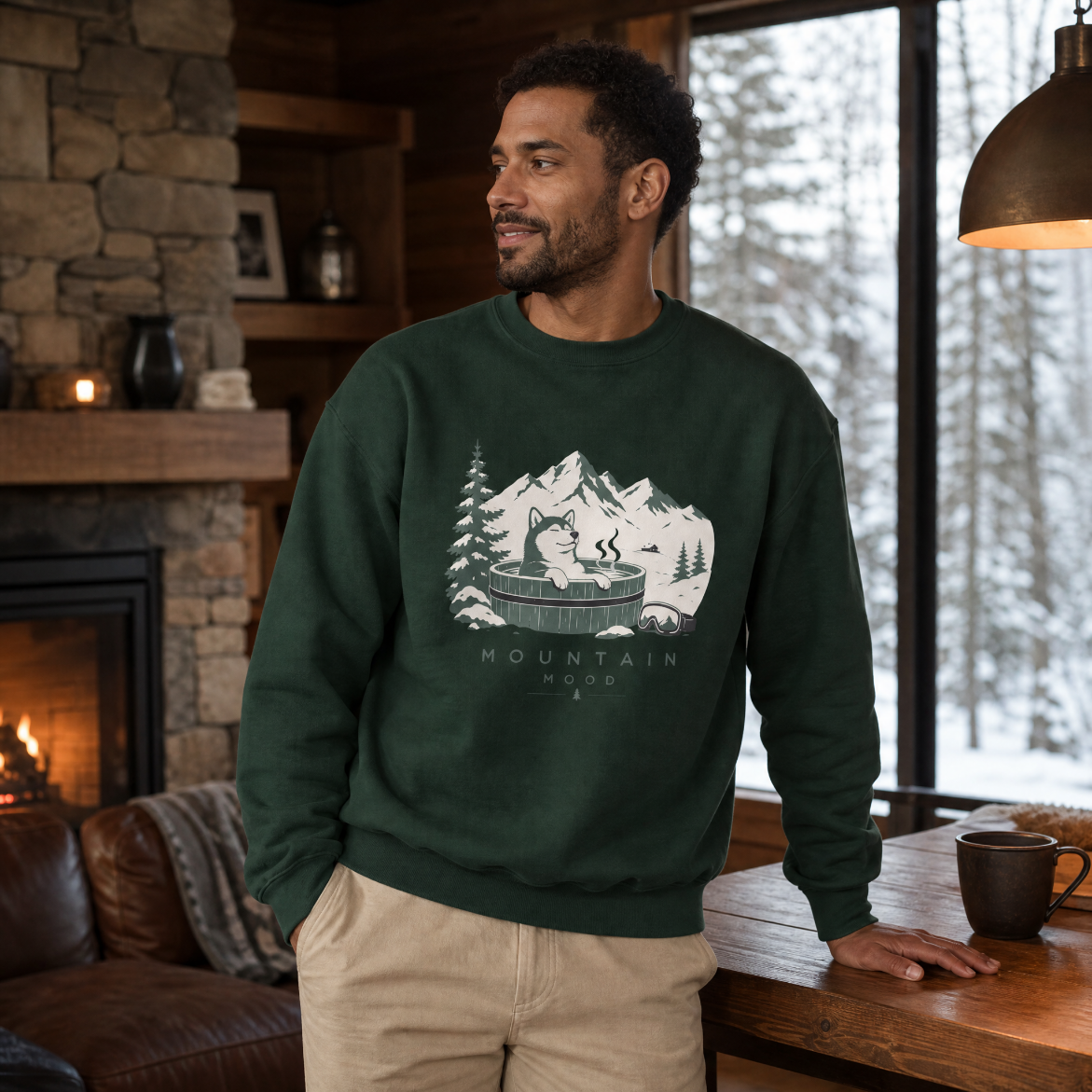 Man wearing a forest green sweatshirt with a mountain graphic in a cozy living room.