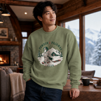 Man wearing a military green sweatshirt with a graphic design in a cozy living room with a fireplace and snowy view.