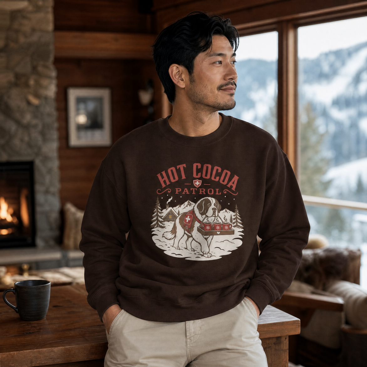 Man wearing a 'Hot Cocoa Patrol' sweater in a cozy room with a fireplace and mountain view.