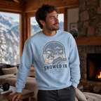 Man wearing a light blue sweatshirt with a mountain and dog graphic, standing in a cozy living room with a fireplace and mountain view.