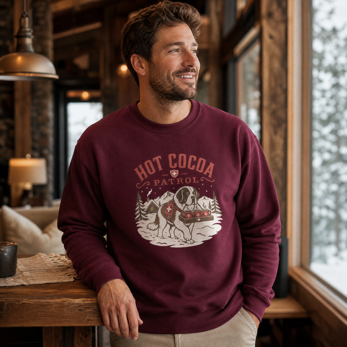 Man wearing a maroon sweatshirt with 'Hot Cocoa Patrol' design in a cozy indoor setting.