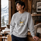 Man wearing a gray sweatshirt with a graphic design in a cozy indoor setting with a window view of mountains.