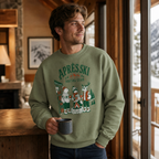 Man wearing a military green sweatshirt with 'Après Ski Social Club' design, holding a mug indoors.